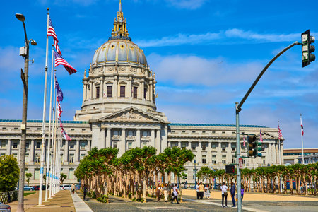 City hall entrance with trees and pedestrian and variety of flags on blue sky day with purple cloudsの写真素材