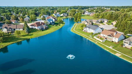 Large pond with water fountain aerial over neighborhood with large expensive houses