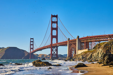 Boulders on sandy beach with waves and seafoam on shoreline to Golden Gate Bridgeの写真素材
