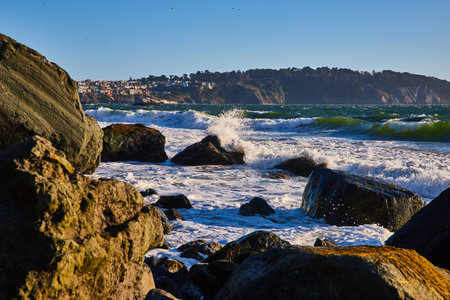Big waves rolling into massive boulders with ocean spray around partially submerged rock