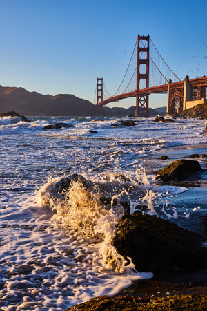 Water spraying around rock in sunset gold with Golden Gate Bridge in backgroundの写真素材