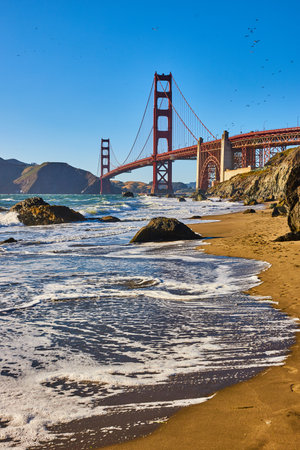 Boulders on sandy beach with crashing waves and seafoam and distant Golden Gate Bridgeの写真素材