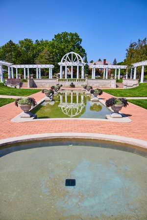 Circular pool with rectangle pool ahead with flowerpots and white pergola and trellises