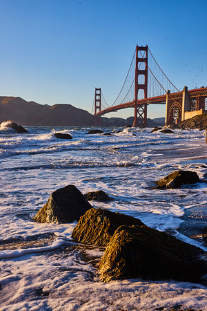 Water frothing around boulders in water at sunset with Golden Gate Bridgeの写真素材