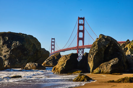 Massive boulders on sandy beach with waves and seafoam along shore to Golden Gate Bridgeの写真素材