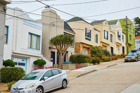 Row of houses beside street going uphill side by side with wires overhead and cars on streetの写真素材