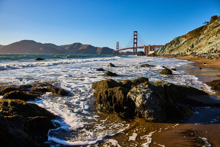 Mossy rocks on sandy beach with waves and seafoam along shore to Golden Gate Bridgeの写真素材
