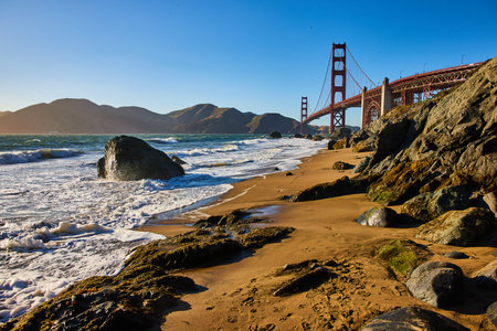 Mossy rocks and waves on beach looking at Golden Gate Bridgeの写真素材