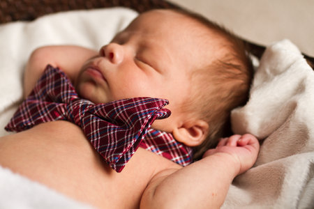 Sleeping Newborn Baby with Plaid Bow Tie on Soft White Blanketの写真素材