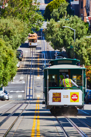 Dust behind green trolley on steep hill tracks with oncoming streetcar on sunny CA dayの写真素材