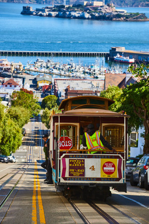 Red and tan trolley streetcar number 4 going downhill toward pier and Alcatraz Island, San Francisco, CAの写真素材