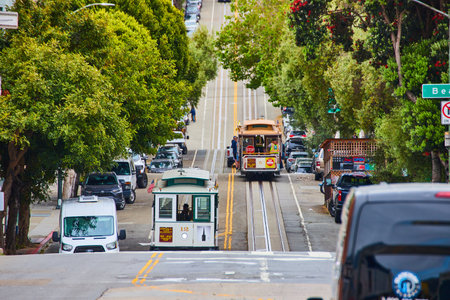 Two trolleys on bumpy hilly road one white and one tan going down a hill, San Francisco, CAの写真素材