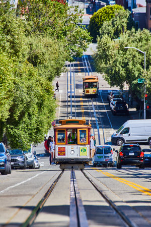 Front of trolley coming up hill at center of shot with cars on road and streetcar on separate tracksの写真素材
