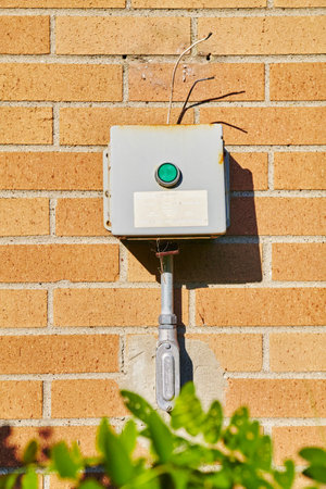 Aged Electrical Junction Box on Brick Wall with Green Foliageの写真素材