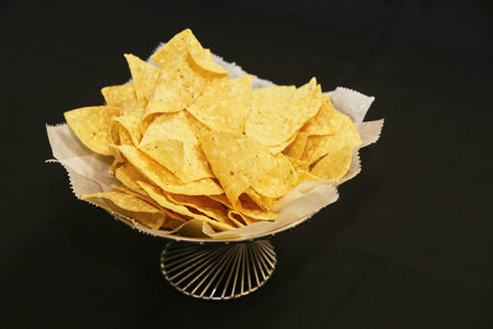Crispy Golden Tortilla Chips in Decorative Bowl Against Black Background