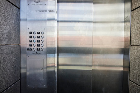 Modern elevator panel with safety features and sleek steel doors, ideal for urban architectural...