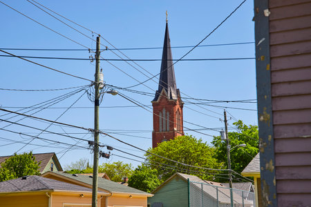 Historic church spire towers over Fort Wayne's vibrant, contrasting urban landscape and modern utilities.の写真素材