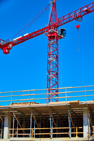 Red crane towers over bustling construction site under a clear blue sky in Downtown Fort Wayne, Indiana.の写真素材