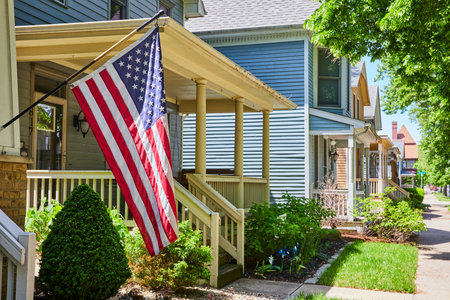 Sunny Suburban Street with American Flag and Lush Gardens, Eye-Level Viewの写真素材