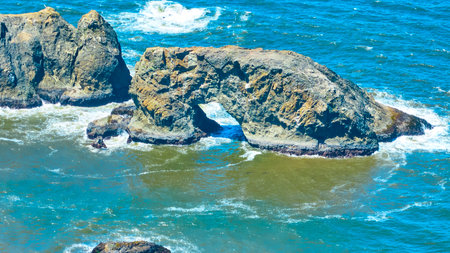 Aerial Fly Through Arch Rock with Crashing Waves in Oregon Coastの写真素材