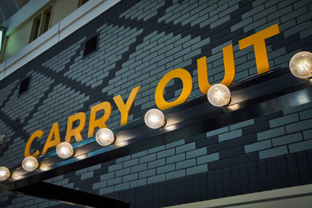 Modern Carry Out Sign on Brick Wall with Warm Night Lighting Low Angle