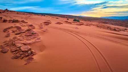 Aerial Tire Tracks on Red Sand Dunes and Rock Formations at Sunrise in Utahの写真素材