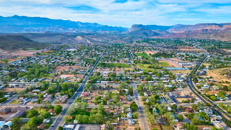 Aerial Small Town Neighborhoods with Red Rock Mountains and Green Trees Fly Overの写真素材