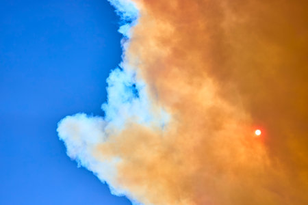 Wildfire Smoke Cloud and Sun Against Blue Sky Environmental Disaster Sceneの写真素材