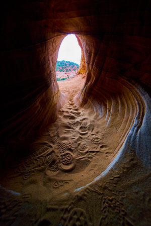 Sandstone Cave Tunnel with Hiker Footprints and Sunlit Utah Desert Entranceの写真素材