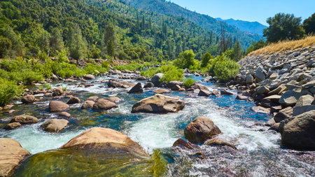 Merced River Flowing Over Rocks with Lush Green Forest and Mountain Hills