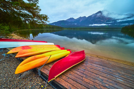 Colorful Canoes and Kayaks on Dock Reflected in Calm Lake with Majestic Mountain Viewの写真素材