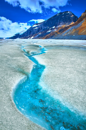 Athabasca Glacier Meltwater Stream and Rugged Mountain Under Blue Skyの写真素材