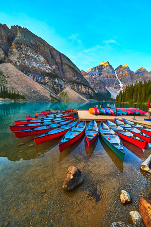 Canoes on Crystal Clear Lake at Sunrise with Rocky Mountains and Evergreen Forestの写真素材