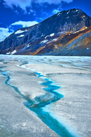 Athabasca Glacier Meltwater Stream and Rugged Mountain Under Blue Skyの写真素材