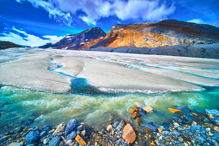 Athabasca Glacier Meltwater Flowing Beneath Rocky Mountain Peaks and Blue Skyの写真素材