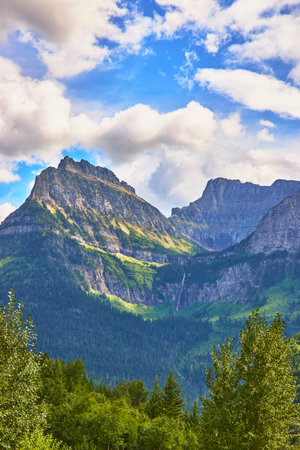 Mountain Peaks Waterfall and Lush Forest Under Blue Skyの写真素材
