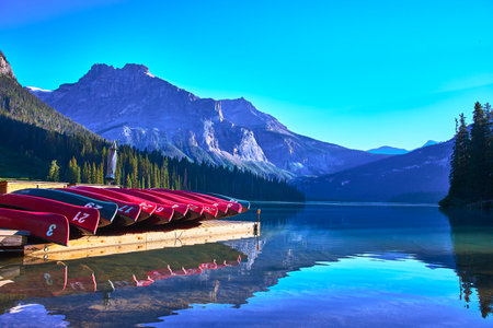 Canoes on Wooden Dock Reflected in Mountain Lake with Pine Forest and Peaksの写真素材