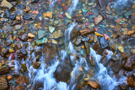 Colorful Riverbed Stones and Flowing Water Cascade in Vibrant Nature Close Upの写真素材