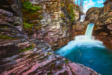 Saint Mary Falls Waterfall and Layered Rock Formations with Vivid Blue Poolの写真素材