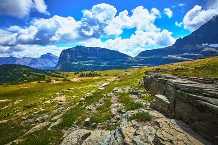 Hidden Lake Trail Rocky Meadow and Majestic Mountain Peaks Under Dramatic Cloudsの写真素材