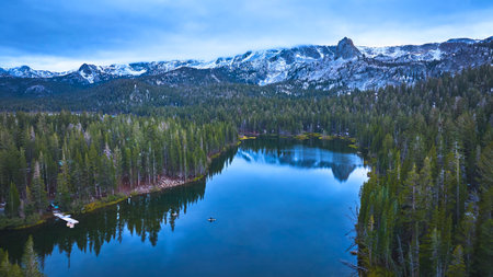 Aerial Pristine Lake Surrounded by Pine Forest and Snowy Mountains in Californiaの写真素材