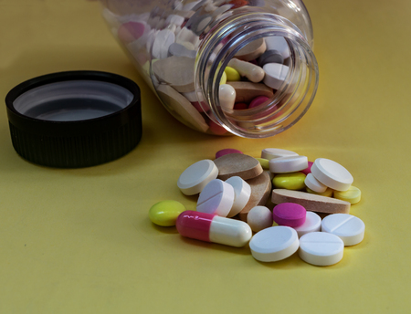 different pills from a bottle on a yellow backgroundの写真素材