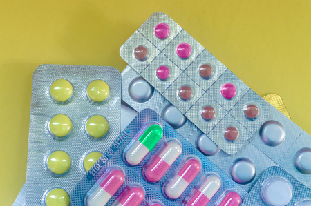 Yellow pills, red white tablets in a package on yellow backgroundの写真素材