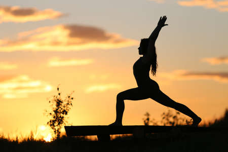 A woman practices yoga at sunset. A silhouette is visible against the sunset.の写真素材