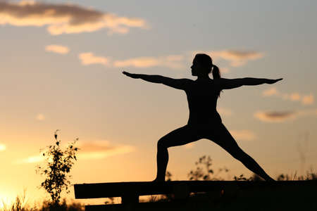 A woman practices yoga at sunset. A silhouette is visible against the sunset.の写真素材