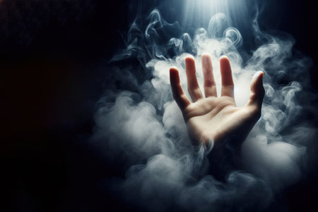 Hand illuminated by light in smoke on dark background. Space for textの素材
