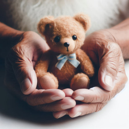 Old man's hands holding a small toy bearの素材