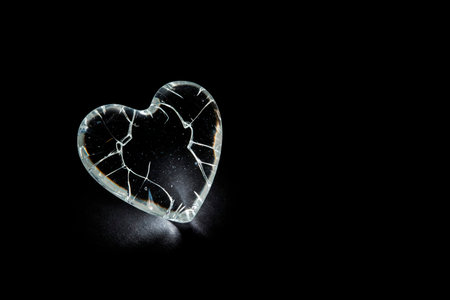 A cracked glass heart on a black background. Space for textの素材