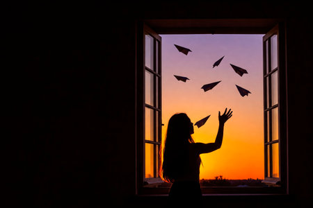 A girl releases paper airplanes out of a window at sunset. Space for textの素材