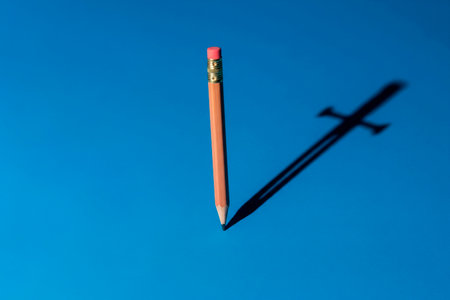 The pencil casts a shadow in the form of a sword on a blue background. Space for textの素材